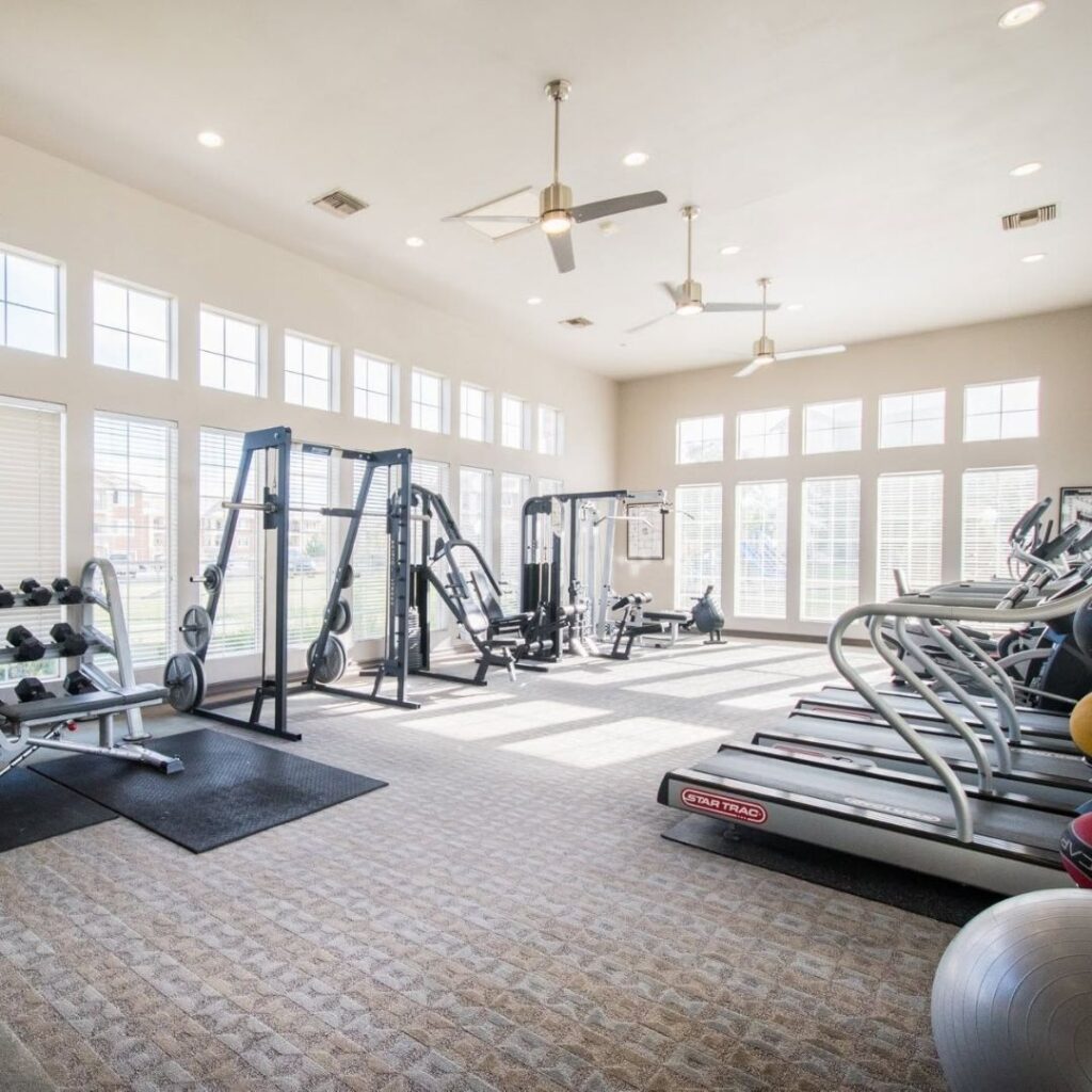 A well-lit, 24-hour fitness center featuring modern cardio machines and a free weight area.